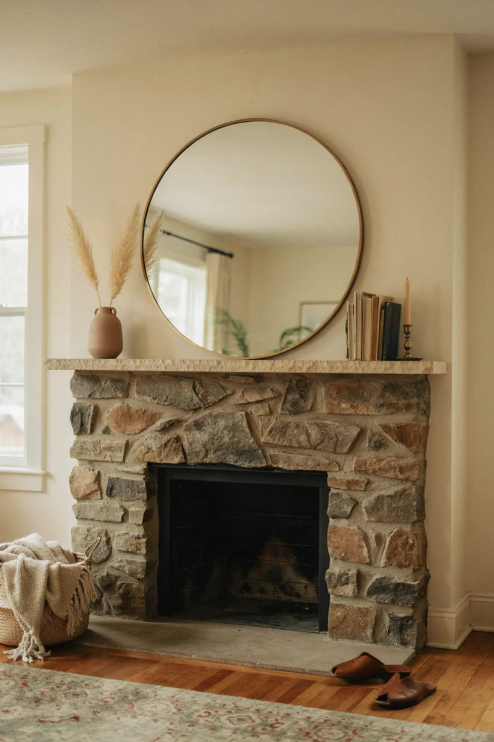 An oversized round mirror hanging above a natural stone fireplace mantel in a cozy living room