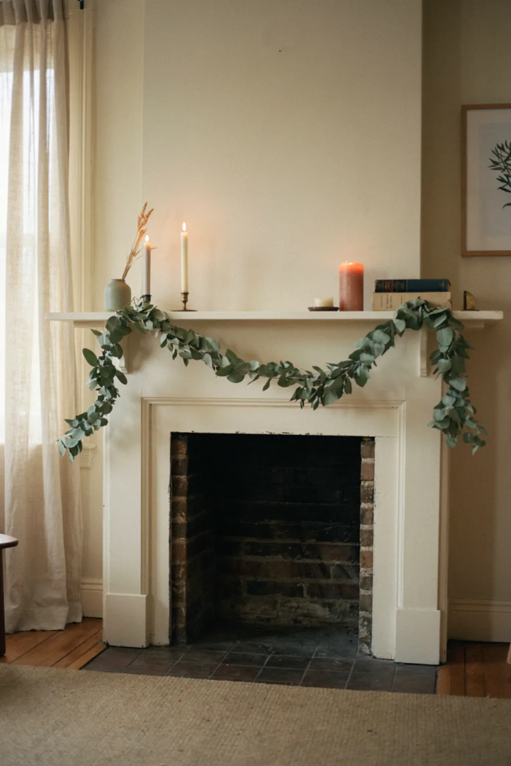A soft eucalyptus garland draped across a white fireplace mantel with a few candles, cozy living room