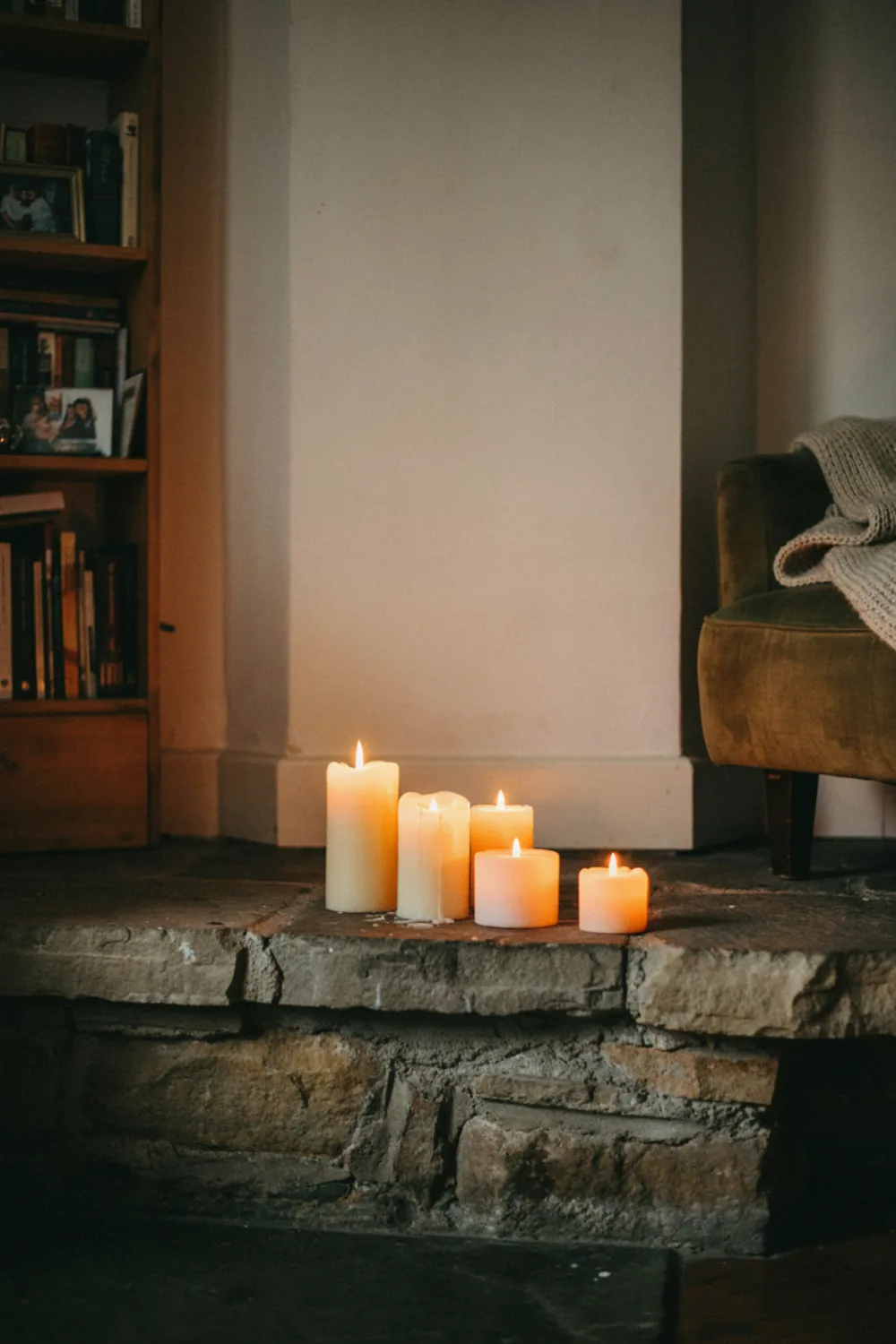A group of cream pillar candles at different heights lit on a fireplace hearth, cozy evening living room