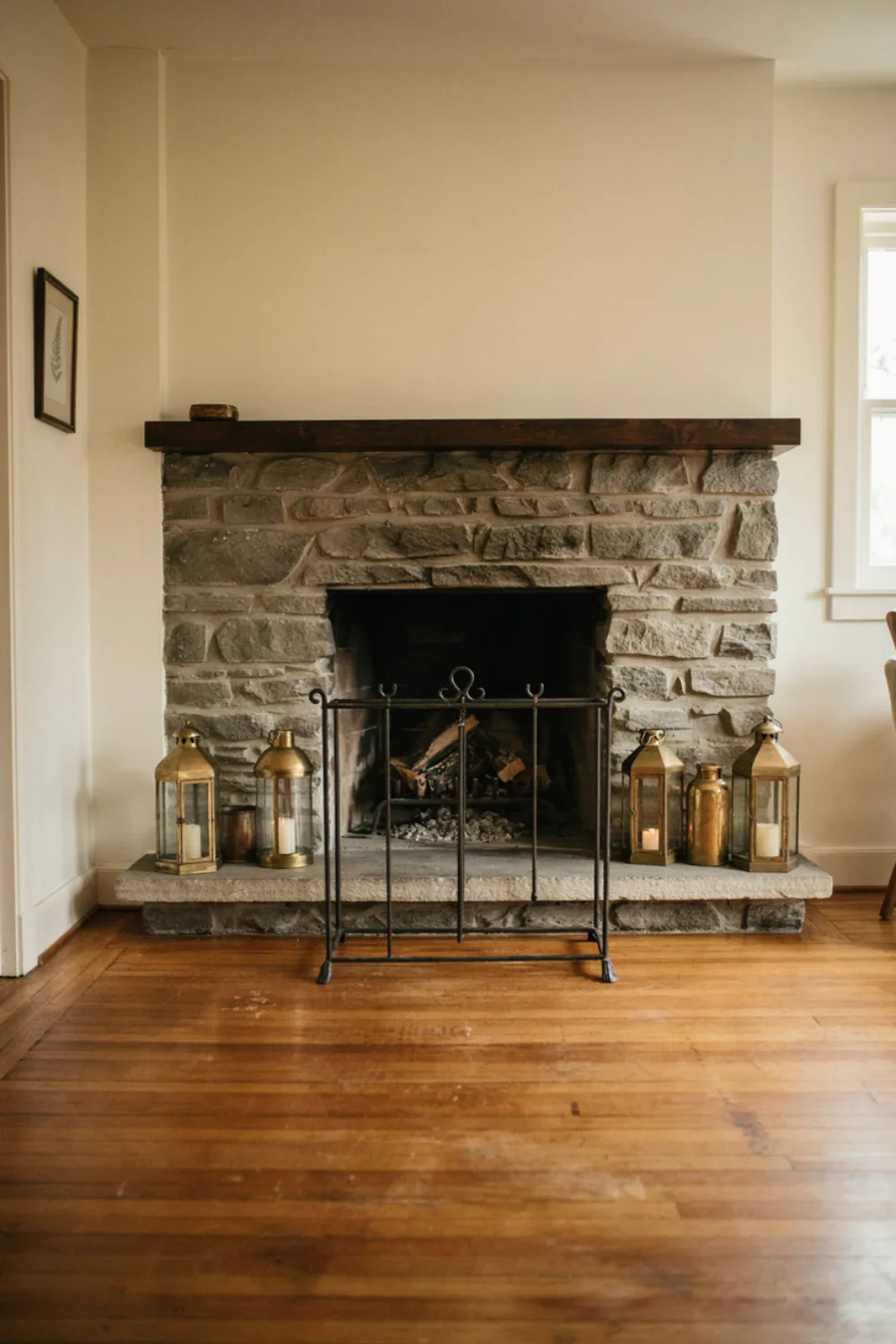 A black metal fire screen standing in front of a fireplace with a row of brass lanterns on the hearth, cozy living room