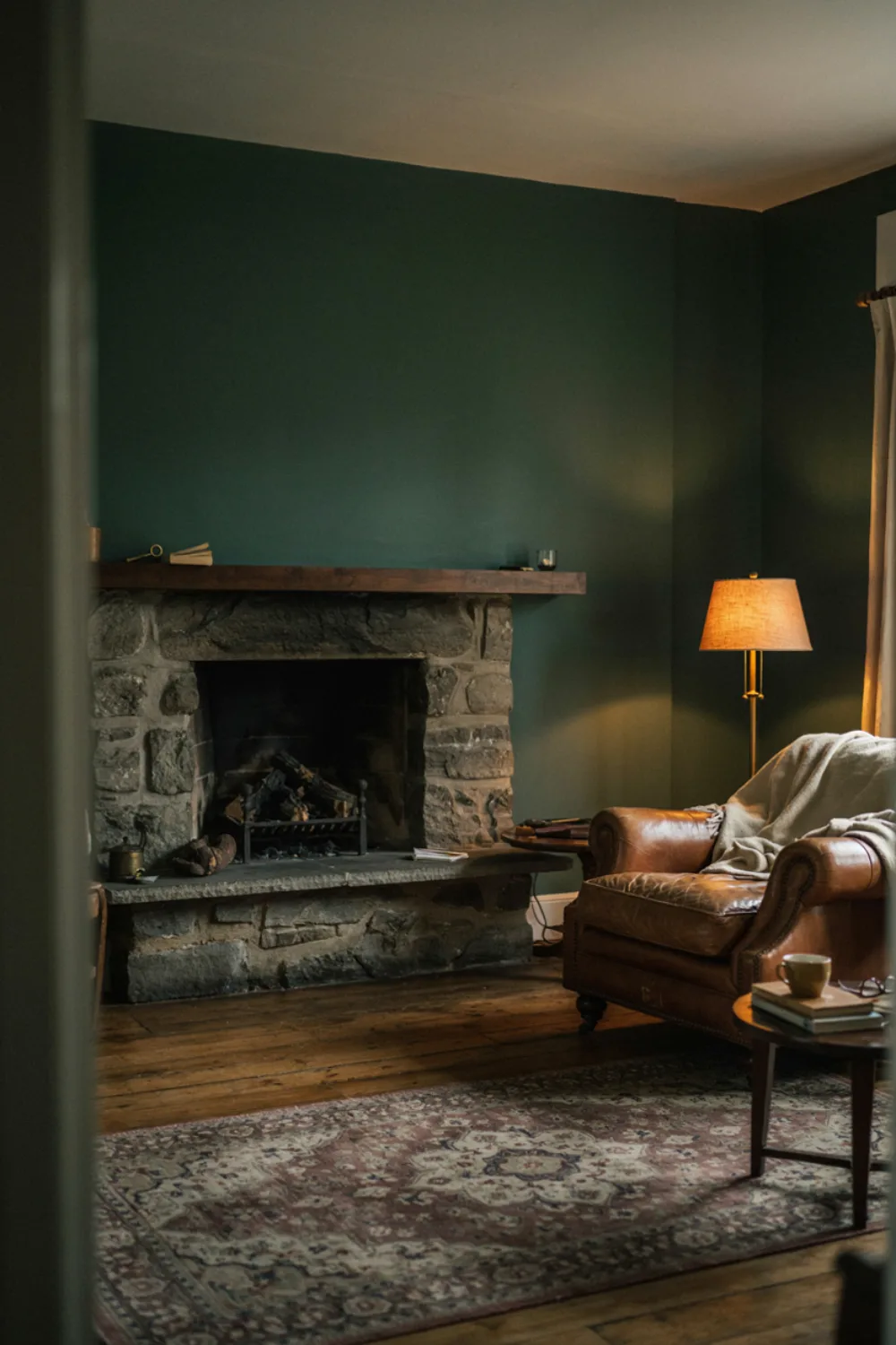 A moody living room with a fireplace wall painted deep forest green, a leather armchair and warm lamp light